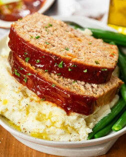 Slices of turkey meatloaf on top of mashed potatoes with green beans.