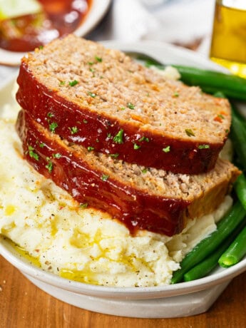 Slices of turkey meatloaf on top of mashed potatoes with green beans.