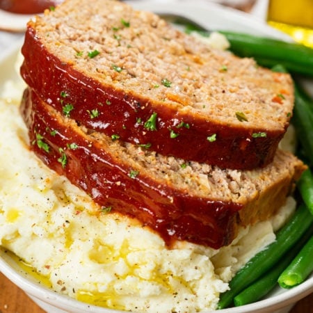 Slices of turkey meatloaf on top of mashed potatoes with green beans.
