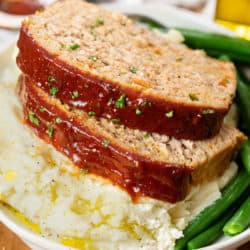 A plate with Turkey Meatloaf on top of a pile of mashed potatoes with green beans.