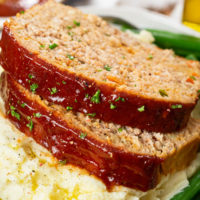 Slices of turkey meatloaf with glaze on top of mashed potatoes.