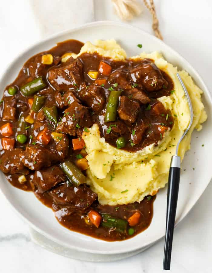 A plate with mashed potatoes topped with Beef Vegetable Soup.