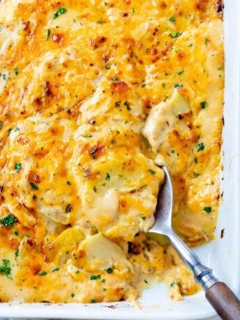 Cheesy Scalloped Potatoes in a casserole dish with a spoon in it.