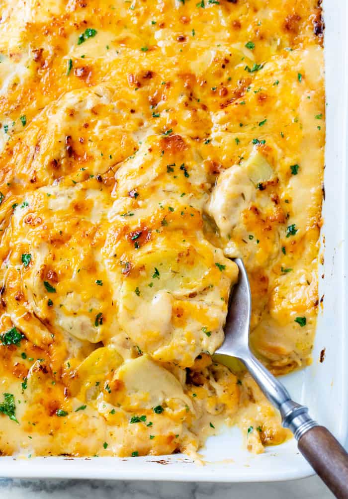 Cheesy Scalloped Potatoes in a casserole dish with a spoon in it.