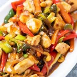 A white platter piled with easy chicken stir fry and vegetables with sauce on it.