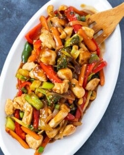 Overhead view of a white platter with chicken stir fry covered in sauce.