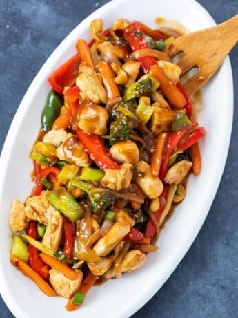 Overhead view of a white platter with chicken stir fry covered in sauce.