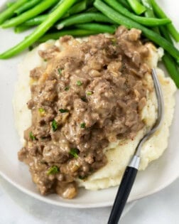 Hamburger Gravy over mashed potatoes with green beans in the background.