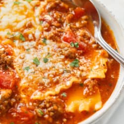 A white bowl filled with Lasagna Soup topped with cheese with a spoon in the back.