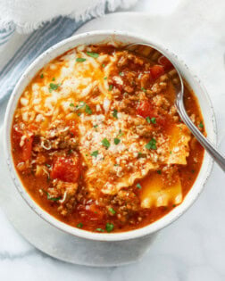 Lasagna Soup in a white bowl with cheese on top and a spoon on the side.