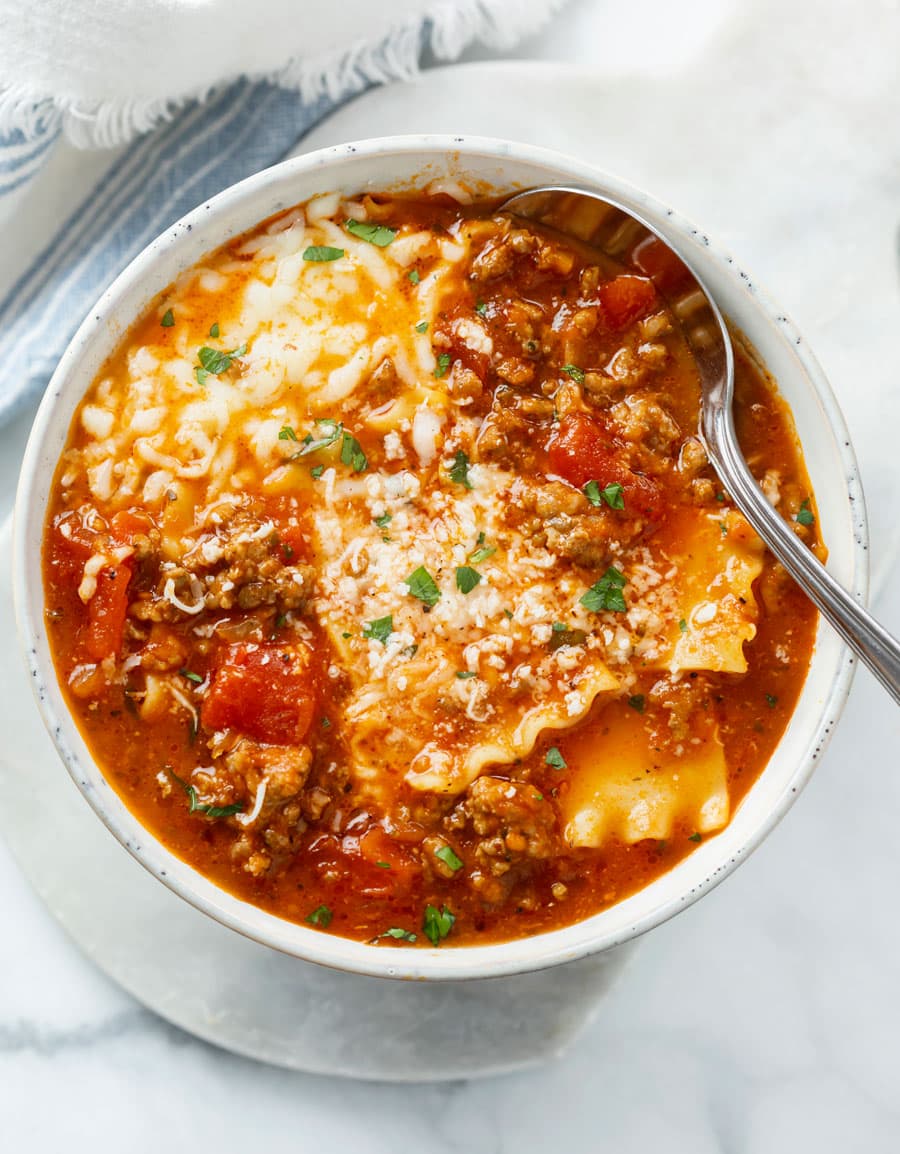 Lasagna Soup in a white bowl with cheese on top and a spoon on the side.