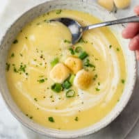 A white bowl full of Potato Leek Soup with a spoon in it and croutons on top.