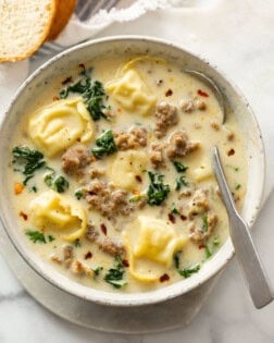 A bowl of creamy sausage tortellini soup with kale and a spoon.