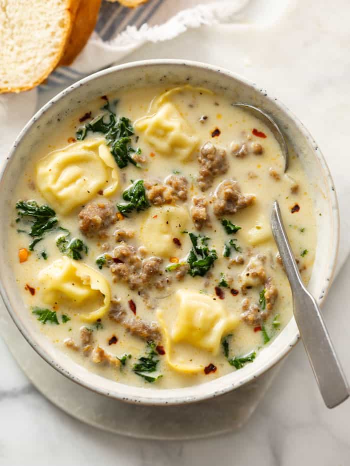 A bowl of creamy sausage tortellini soup with kale and a spoon.