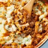 A wooden spoon scooping up Skillet Lasagna with a meat sauce and cheese on top.