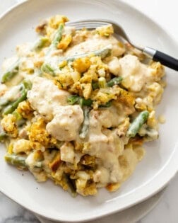 A white plate with Chicken and Stuffing Casserole and green beans with a fork.