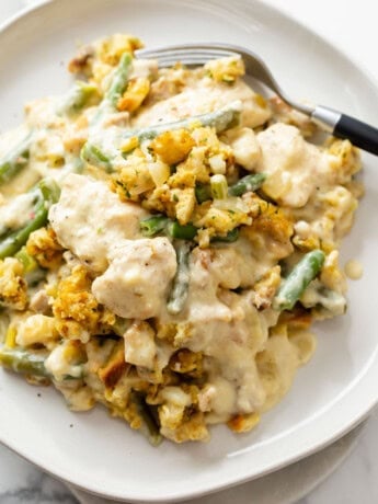 A white plate with Chicken and Stuffing Casserole and green beans with a fork.