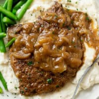 Cube Steak smothered in brown gravy with onions on a pile of mashed potatoes.