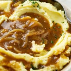 A bowl of creamy mashed potatoes topped with brown onion gravy.