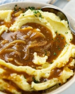 A bowl of creamy mashed potatoes topped with brown onion gravy.