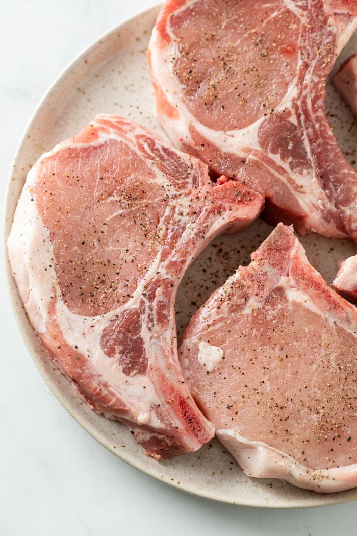 A plate with bone-in Pork Chops with marbled meat for making Pork Chops in Gravy