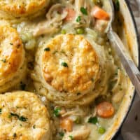 A skillet of Chicken Pot Pie with flaky biscuits on top and fresh parsley.