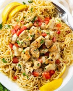 A white platter filled with Chicken Scampi with angel hair pasta and diced tomatoes with lemons and parsley.