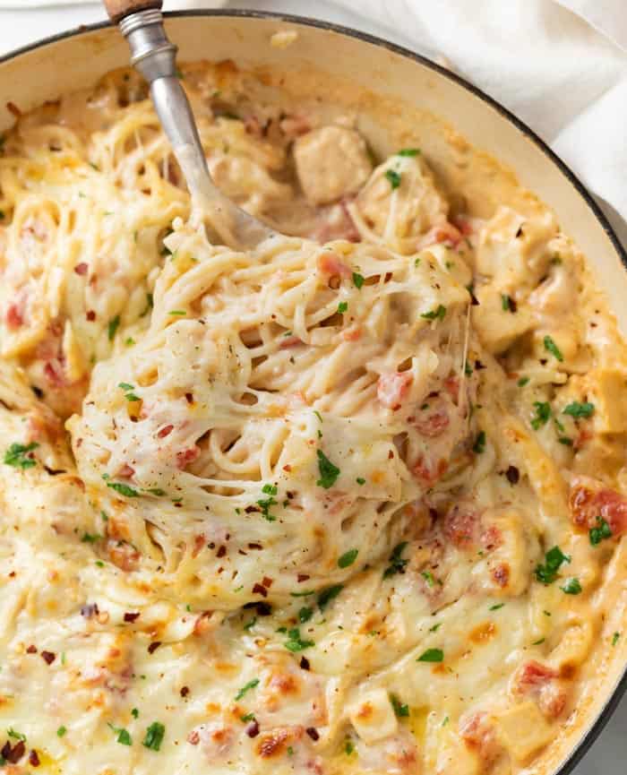 A casserole dish filled with cheesy Chicken Spaghetti with a spoon pulling it up.