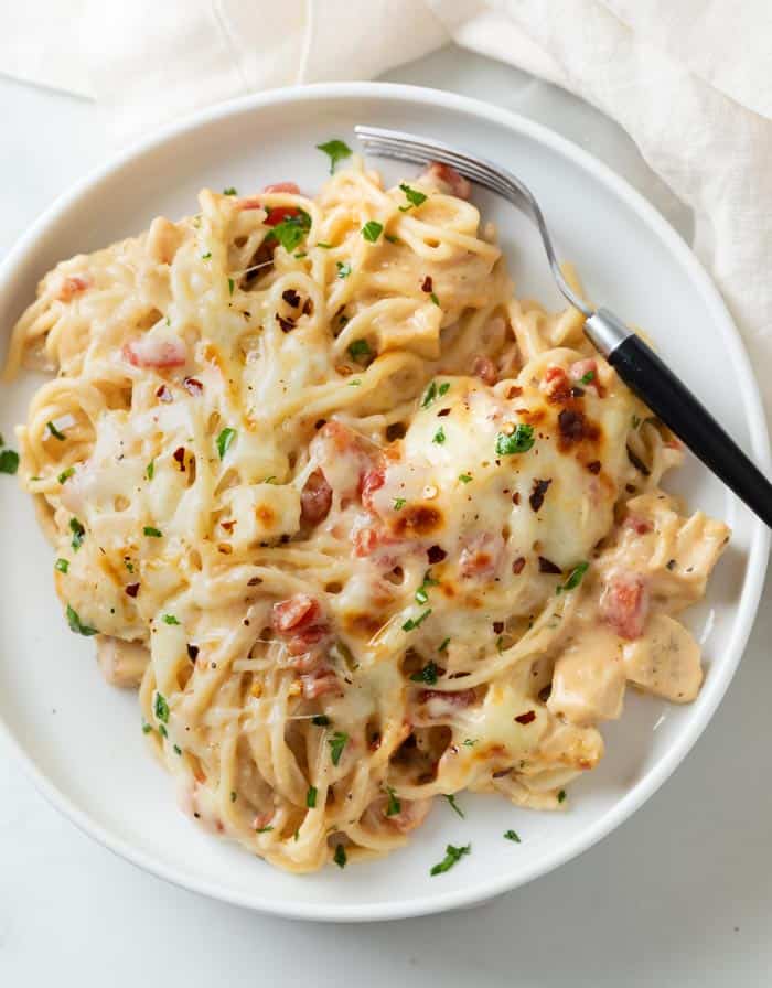 A white plate topped with creamy Chicken Spaghetti topped with red pepper flakes and parsley.