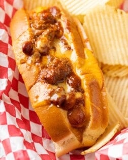 A Chili Cheese Dog in a red serving basket with potato chips.