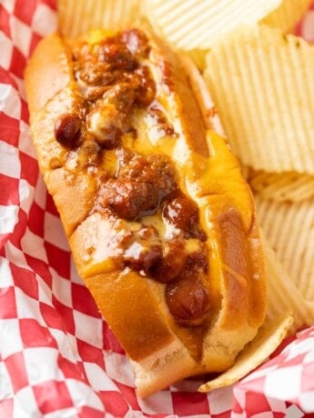 A Chili Cheese Dog in a red serving basket with potato chips.