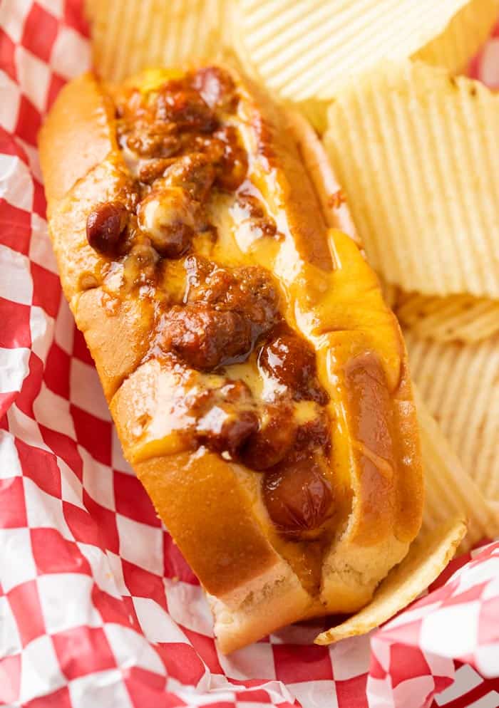 A Chili Cheese Dog in a red serving basket with potato chips.