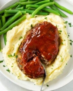 Mini Meatloaf topped with glaze on a pile of mashed potatoes with green beans.