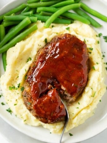 Mini Meatloaf topped with glaze on a pile of mashed potatoes with green beans.