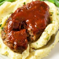 A mini meatloaf on top of mashed potatoes with a fork slicing into it.