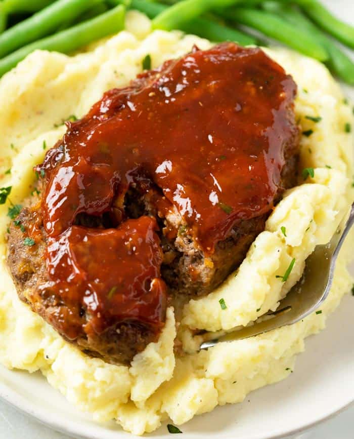A mini meatloaf on top of mashed potatoes with a fork slicing into it.