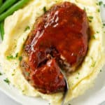A mini meatloaf with glaze on a pile of mashed potatoes with parsley.