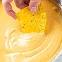 A hand dipping a tortilla chip into a skillet of Nacho Cheese Sauce.