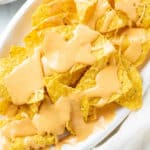 A pile of Tortilla Chips with creamy Nacho Cheese Sauce on top.