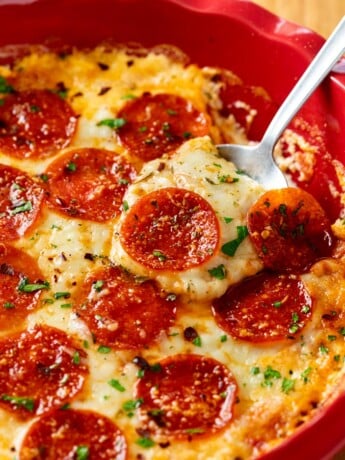 A spoon scooping up cheesy Pizza Dip with mozzarella cheese and Pepperoni.