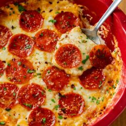A red pie plate filled with pepperoni Pizza Dip with a spoon in it.