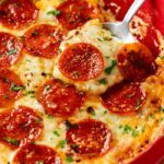 A spoon holding warm Pizza Dip topped with melted cheese and Pepperoni.