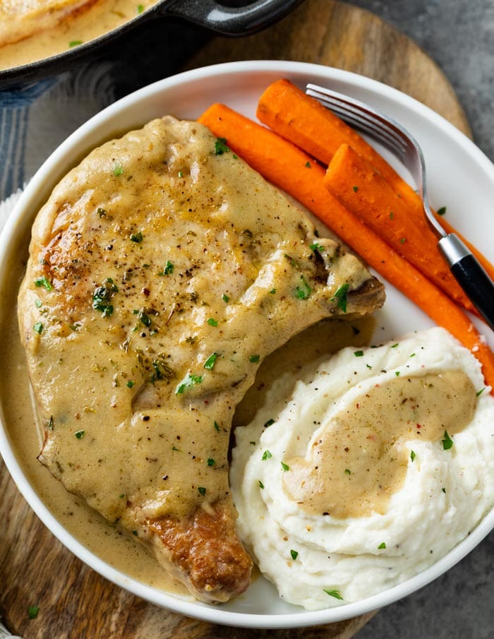 A white plate with Pork Chops in Gravy with carrots and mashed potatoes.