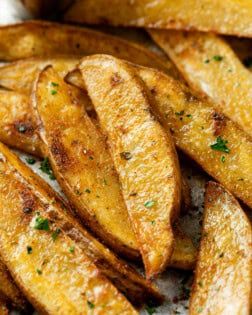 A pile of Baked Potato Wedges topped with parsley and seasoning.