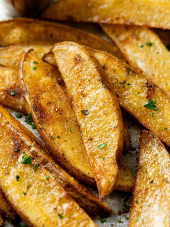 A pile of Baked Potato Wedges topped with parsley and seasoning.