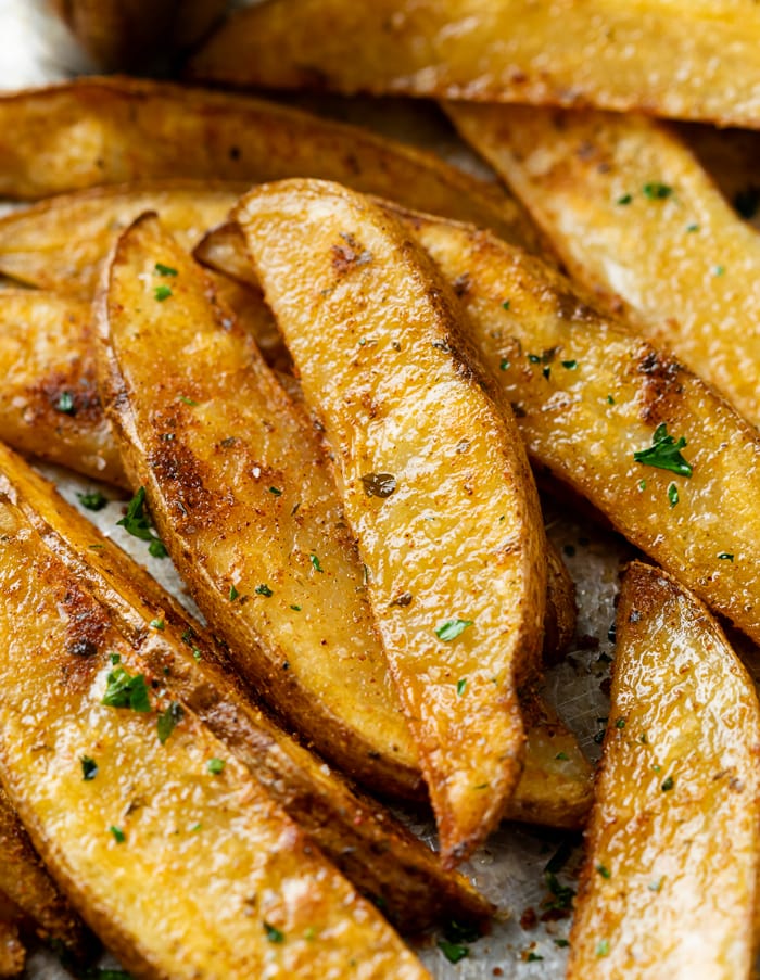 A pile of Baked Potato Wedges topped with parsley and seasoning.