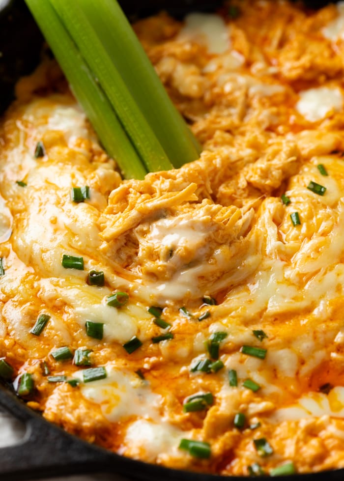 Creamy Buffalo Chicken Dip with Chives on top and bleu cheese dressing with celery sticks in the back.