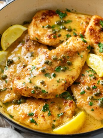 A pot with crispy Chicken Piccata in a white wine butter sauce with lemon wedges and capers.