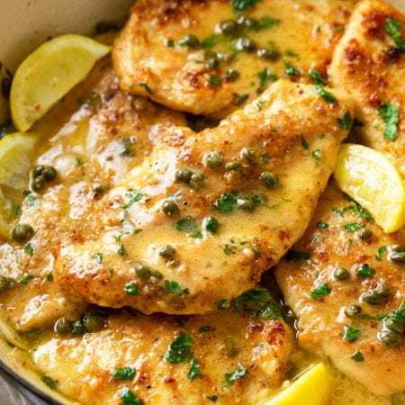 A pot with crispy Chicken Piccata in a white wine butter sauce with lemon wedges and capers.