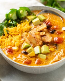 Chicken Tortilla Soup in a soup bowl with colorful toppings and a spoon in the back.